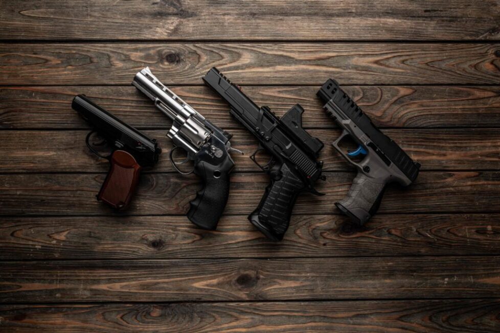 Four different handguns displayed side by side on wooden planks.